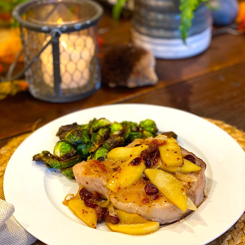Pork Chops with Apples and Cranberries ready to eat. This delicious pork chop is piled high with cooked apples, onions and cranberries in a delicious gravy.