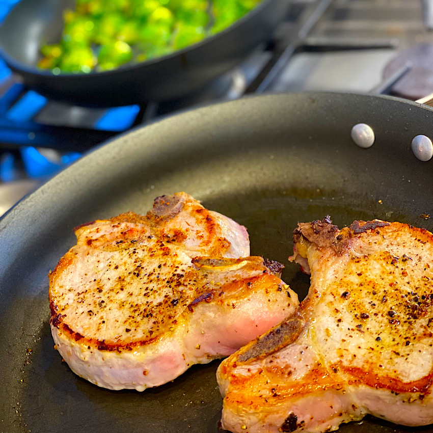 Two large pork chops browning in a pan.