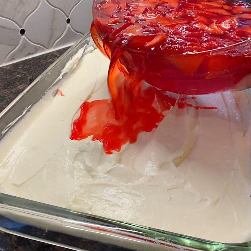 Pouring on the strawberry jello and fresh strawberry layer to the Strawberry Pretzel Salad.